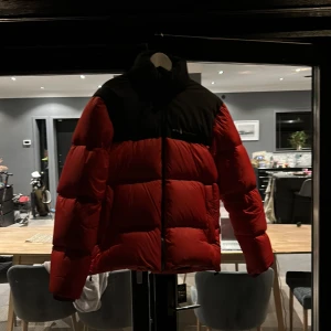 Röd och svart pufferjacka från Sail Racing - Säljer en snygg röd och svart pufferjacka från Sail Racing. Jackan har en hög krage och dragkedja framtill. Perfekt för kyliga dagar med sin vadderade design.