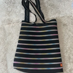 Randig axelväska med dragkedjor - Snygg axelväska med ett unikt randigt mönster i flera färger. Mått 42 *37 cm utan handtag.Väskan har flera dragkedjor som ger en cool och modern look. Perfekt för att bära med sig det nödvändigaste med stil.