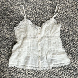 Vit topp från Zara - Säljer en söt vit topp från Zara med spetsdetaljer och knappar framtill. Har aldrig använt den🤍