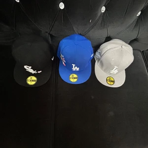 Tre kepsar - Säljer tre stilrena kepsar med broderade logotyper. En svart keps med vit logotyp och hjärtdetalj, en blå keps med vit logotyp och broderade detaljer, samt en grå keps med vit logotyp. Perfekta för att komplettera din streetwear-look.