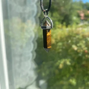 Halsband med tigeröga-pendel - Snyggt halsband med en tigeröga-pendel i en silverfärgad infattning. Hängsmycket har en unik, naturlig mönstring i brunt och guld. Kedjan är svart och justerbar med ett klolås. Perfekt för att ge en bohemisk touch till din stil.