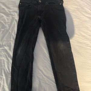 Svarta jeans från h&m  - Säljer ett par svarta h&m jeans med relaxed fit och tapered ben. Klassisk design med fem fickor och knappgylf. Perfekta för en avslappnad stil.