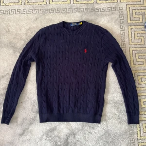 Marinblå kabel stickad tröja från Polo Ralph Lauren - Säljer min kabelstickade Ralph Lauren tröja, Storlek M, har inte haft möjligheten att ha på mig den så mycket. Axelbredden är 46cm, längden är 70cm.