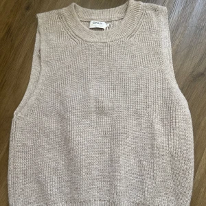 Beige stickad väst från ONLY - Säljer en stilren beige stickad väst från ONLY. Perfekt för lager-på-lager och har en ribbad kant vid halsen och ärmhålen. En mångsidig och bekväm väst för alla tillfällen.