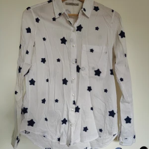 Vit skjorta med stjärnmönster - Säljer en vit skjorta med blå stjärnor. Skjortan har långa ärmar och knappar framtill samt en bröstficka. Perfekt för en unik och stilren look.