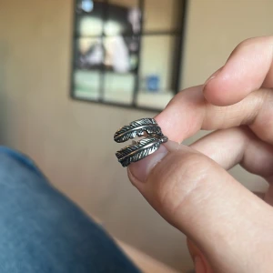 Silverfärgad ring med fjäderdesign - Snygg silverfärgad ring med en unik fjäderdesign.  Ringen är i storlek 5 och har en elegant och modern look. Material rostfritt stål och pris går även att diskutera