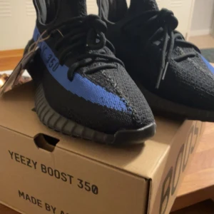Yeezy 350 Dazzling Blue - Ett par Yeezy 350 Dazzling Blue i bra skick! Självklart äkta och köpta för runt 4000 SEK cirka 7 månader efter att de släpptes år 2022. Skorna är sparsamt använda, ena skosnöret är lite sönder (se sista bilden) annars i utmärkt skick för att ha haft dom sen 2022! Kvitto finns om man vill se! Mvh