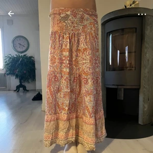 Mönstrad långkjol från Marta - Säljer en färgglad långkjol från Marta med ett vackert paisleymönster i rött, orange och beige. Kjolen har en elastisk midja för en bekväm känsla.