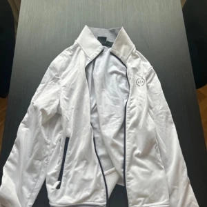 Vit jacka från Armani Exchange - Snygg vit jacka från Armani Exchange med dragkedja och stilrena detaljer. Perfekt för en sportig look. Jackan har långa ärmar och en diskret logga på bröstet.