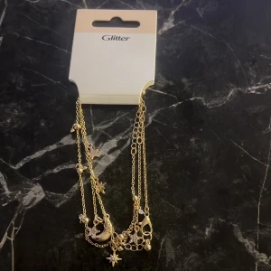 Guldarmband med stjärnor och måne från Glitter - Elegant guldarmband från Glitter med hängande stjärnor och måne. Perfekt för att lägga till en touch av magi till din outfit. Kedjan är tunn och smidig, vilket gör den lätt att bära hela dagen.