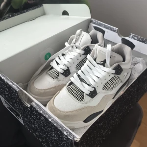 Air Jordan 4 Retro (GS) i vit och grå - Säljer ett par stilrena Air Jordan 4 Retro (GS) sneakers i vit och neutral grå. Skorna har en klassisk design med snörning och detaljer i svart. Perfekta för dig som älskar en tidlös look.