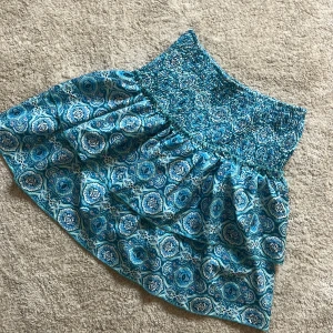 Blå mönstrad kjol - Säljer en blå mönstrad kjol med elastisk midja. Kjolen har ett vackert mönster i olika blå nyanser och en luftig passform. Perfekt för varma dagar!