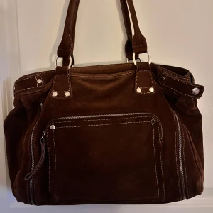 Brun mockaväska från Longchamp - Säljer en snygg brun mockaväska från Longchamp med flera dragkedjor och praktiska fack🤎
