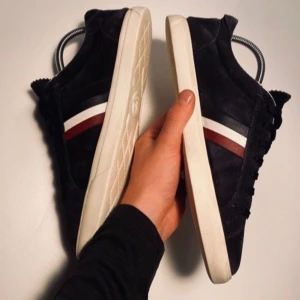 Blåa sneakers från Moncler - Snygga Blåa sneakers från Moncler med vita och röda ränder på sidan. Skorna har en vit sula och är tillverkade i mocka. Perfekta för en stilren look.