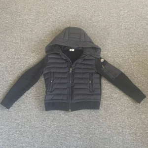 Marinblå cardigan med huva från Moncler - Snygg marinblå cardigan från Moncler med huva och dragkedja. Jackan har långa ärmar i ribbat material och praktiska fickor.