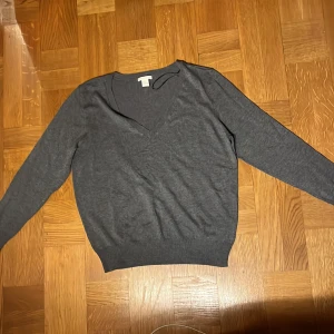 Grå tröja med v-ringning från HM - Säljer en stilren grå tröja från HM med v-ringning. Tröjan har långa ärmar och är perfekt för en avslappnad look. Den är tillverkad i ett mjukt material som känns skönt mot huden. Passar bra till både jeans och chinos.