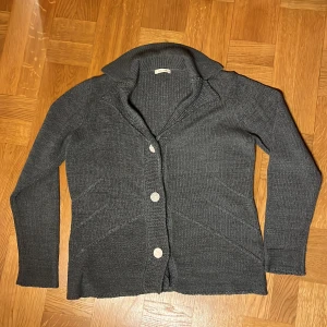 Grå stickad kofta från Intown - Säljer en stilren grå stickad kofta från Intown. Koftan har långa ärmar och knäpps med knappar framtill. Perfekt för kyliga dagar och ger en mysig känsla. Passar bra till både jeans och kjol.