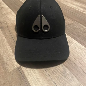 Äkta keps  - Snygg svart keps  med en unik metallogo framtill. Kepsen har justerbart spänne baktill för perfekt passform. Perfekt för en stilren look.