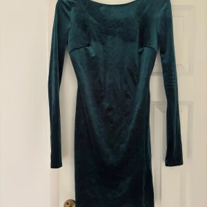 Mörkgrön långärmad sammetsklänning - Snygg mörkgrön klänning i mjuk sammet med långärmad design och kroppsnära passform. Klänningen har en enkel, stilren look med rundad hals och är perfekt för dig som gillar klassiska vibes med en modern twist. Fårn Nelly 
