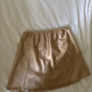 Champagnefärgad satin kortkjol - Snygg kortkjol i champagnefärgad satin med mjukt fall och resår i midjan. Perfekt för dig som gillar en enkel men lyxig look. Kjolen har en lätt glansig yta och är superenkel att matcha med både toppar och sneakers.