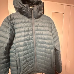 Mörkgrön dunjacka med huva - Säljer en mörkgrön dunjacka med snygg quiltad design och stor huva. Jackan har dragkedja framtill och två sidofickor. Perfekt för kalla dagar och har en clean, modern look som passar till streetwear. Jackan är långärmad och har en loose passform.