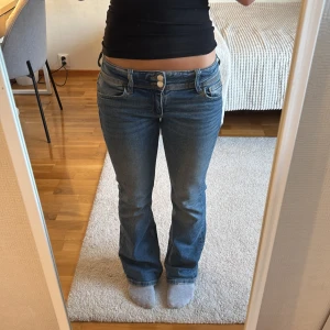 Blå bootcut jeans Gina Tricot - Snygga blå bootcut jeans från Gina Tricot med låg midja och klassiska fickor både fram och bak. Jeansen har dubbla knappar i midjan och är tillverkade i ett mjukt bomullsmaterial med lite stretch. 