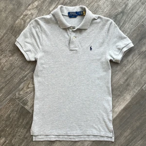 Grå Raulph Lauren Piké - Säljer denna sköna pikén från Raulph Lauren då den börjar bli för liten, storlek L i barnstorlek. Har använts jätte få gånger men är i helt nytt skick. Den är köpt från Kidsbrandstore (Nypris 995kr) och den är slim fit🍾👀✌️.