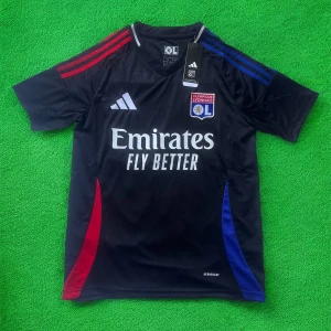 Olympique Lyonnais Adidas matchtröja - Snygg Olympique Lyonnais fotbollströja från Adidas med klubbmärke på bröstet och Emirates-sponsring. Tröjan är svart med röda och blå detaljer på axlar och sidor, samt vita loggor. Tillverkad i lätt och ventilerande polyester med AEROREADY-teknologi. Perfekt för fotbollsplanen.