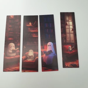 Spökiga bokmärken – set om 4 - Fyra bokmärken med söta spöken som läser böcker i mysiga biblioteksmiljöer. Perfekt för dig som älskar böcker, fantasy och vill ha en unik touch till din läsning. Passar både unga och unga vuxna som vill göra läsningen roligare! Skick: oanvända. Färger verkar ha överfört från ena bokmärket till ett annat baksida. Är fläckigt på baksidan. 