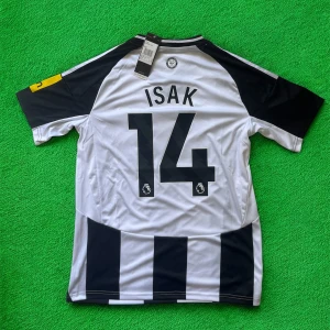 Newcastle Isak 14 Adidas matchtröja - Snygg Newcastle United fotbollströja med Isak och nummer 14 på ryggen. Klassisk svartvit randig design, officiell Premier League-tryck, Adidas-logga och klubbmärke på bröstet. Kortärmad och tillverkad i lätt, ventilerande polyester med Aeroready-teknologi.