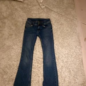 Blå bootcut jeans från RYVLS - Snygga blå bootcut jeans från RYVLS med klassiska fickor bak och coola detaljer som knappar med stjärnmotiv. Jeansen har en låg midja och är gjorda i mjukt denimtyg som sitter skönt hela dagen.