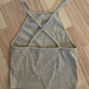 Grå ribbad croppad linnetopp - Snygg grå ribbad linnetopp med smala axelband som korsas i ryggen. Toppen är croppad och har en enkel, stilren design💕