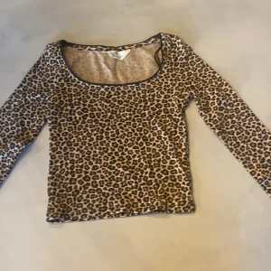 Leopardmönstrad långärmad topp H&M - Snygg långärmad topp från H&M med leopardmönster i beige och bruna toner. Modellen har rundad urringning med svart kant och är tillverkad i ett mjukt, stretchigt material som sitter skönt på kroppen. Perfekt för dig som vill sticka ut med ett djurmönster.