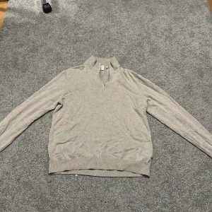 Beige half zip tröja från Bläck - Stilren beige tröja från Bläck med half zip-dragkedja och hög krage. Långärmad modell i mjuk bomull, perfekt för lager-på-lager. Ribbstickade muddar vid ärmslut och nederkant ger en clean look. Passar dig som gillar enkel och snygg stil.
