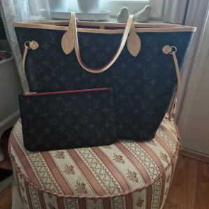 Louis Vuitton Neverfull MM Monogram handväska - Säljer en ny Louis Vuitton Neverfull MM handväska i monogram canvas med beige läderdetaljer och röd randig insida. Väskan har guldiga metalldetaljer, innerficka med dragkedja och medföljande clutch. Perfekt för dig som vill ha en ikonisk och rymlig väska. Det kommer 2 kvitton med väskan och den originella Louis Vuitton boxen med LV dust bag, LV handväskan är köpt år 2025. Väskan har en scannble RFID-TAG som har väskans serial number. Om du är intresserad så skicka meddelande💬