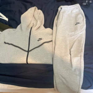 Grå mjukisbyxor från Nike - Snygga ljusgrå mjukisbyxor från Nike med svart logga på låret. Byxorna har resår och snörning i midjan samt sidofickor. Perfekta för chill eller träning, tillverkade i mjukt bomullsmaterial för maximal komfort.