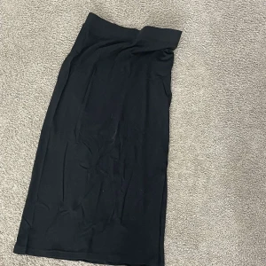 Svart långkjol i mjukt tyg - En stilren svart långkjol med rak passform och bred linning. Kjolen är enkel och tidlös, perfekt för dig som gillar minimalistisk stil. Materialet känns mjukt och följsamt mot huden. Passar dig som vill ha en klassisk look.