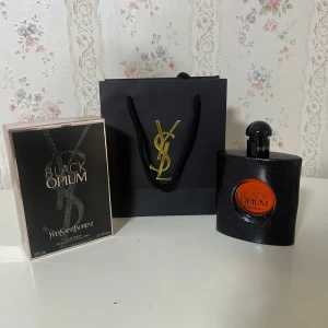 YSL Black Opium Eau de Parfum 90ml - YSL Black Opium Eau de Parfum 90ml med lyxig svart glittrig flaska och rund orange detalj framtill. Kommer med originalkartong och elegant svart presentpåse med guldigt YSL-logo. Doften är ikonisk och passar dig som gillar djärva, moderna parfymer.