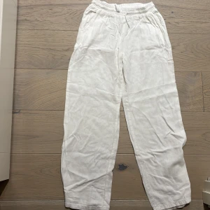 Vita linnebyxor från Lindex, stl 152 - Snygga och luftiga vita linnebyxor från Lindex med resår i midjan och raka ben. Perfekta för varma dagar och chill vibes. Byxorna har sidfickor och är gjorda i ett mjukt linnematerial som känns skönt mot huden.