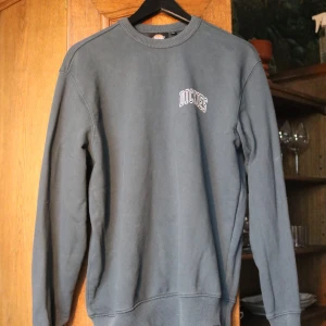 Mörkgrå/blå sweatshirt från Dickies - Snygg mörkgrå/blå sweatshirt från Dickies i storlek XS. Tröjan har rund halsringning, långa ärmar och vit/svart Dickies-logga på bröstet. Tillverkad i mjuk bomullsmix med ribbade muddar vid ärmslut och nederkant. Perfekt för en chill och stilren look.