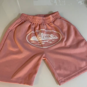 Rosa shorts med tryck och resårmidja - Snygga rosa shorts med elastisk midja och ett vitt tryck framtill. De har en avslappnad passform, sidofickor och en bakficka. Perfekta för varma dagar och chill vibes. Materialet känns mjukt och skönt mot huden.