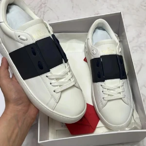Valentino Garavani vita sneakers med svart band - Snygga vita sneakers från Valentino Garavani med ett brett svart band över vristen. Skorna har rund tå, platt sula och klassisk snörning. Perfekta för dig som gillar stilrena och exklusiva detaljer.