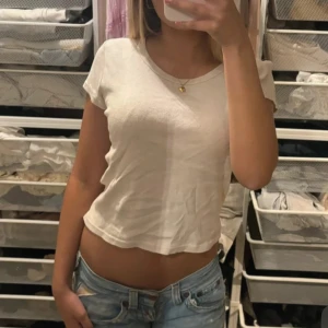 Vit croppad t-shirt - Enkel och fräsch vit croppad t-shirt med korta ärmar och rund halsringning. Perfekt till jeans eller kjol för en avslappnad look. Tunt och mjukt material som känns skönt mot huden.