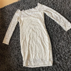 Vit spetsklänning från Acevog - Säljer en vit kortklänning från Acevog med långärmade ärmar och offshoulder-design. Klänningen är täckt av vacker spets med blommigt mönster och har en tight passform som framhäver figuren. Perfekt för dig som vill ha en romantisk och stilren look.