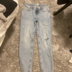 Ljusblå  jeans med raka ben - Säljer ett par ljusblå jeans med snygga slitningar på benen och klassisk femficksdesign. Jeansen har raka ben och rätt baggy