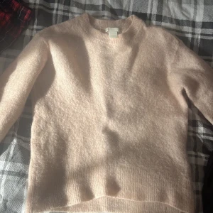 Ljusrosa tröja  - Mysig ljusrosa stickad tröja med rund halsringning och långa ärmar. Tröjan har en fluffig och mjuk känsla, perfekt för lager-på-lager under kyliga dagar. Enkel och stilren design som är lätt att matcha med olika outfits.