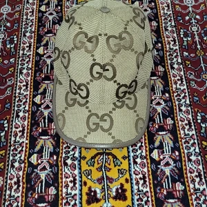 Beige keps från Gucci med GG-mönster - Snygg beige keps från Gucci med det klassiska GG-monogrammet i brunt över hela kepsen. Kepsen har böjd skärm och är tillverkad i ett slitstarkt tyg med detaljer i brunt runt kanterna. Perfekt för dig som vill sticka ut med en ikonisk accessoar.