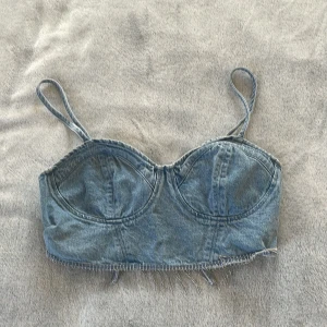 Jeanstopp med fransar i metall - Säljer en snygg jeanstopp från H&M Divided med tunna axelband och fransig nederkant. Toppen har markerade kupor och snörning i ryggen.