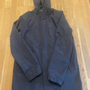 Mörkblå parkajacka från GANT, M - Säljer en mörkblå parkajacka från GANT med huva och dragkedja. Jackan har ett stilrent yttertyg i polyester och ett rutigt foder på insidan. Perfekt för dig som vill ha en clean och funktionell look med snygga detaljer och klassisk passform.