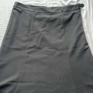 Svart långkjol från Isolde, stl 44 - Klassisk svart långkjol från Isolde i storlek 44. Kjolen har en rak och stilren siluett med dold dragkedja och knapp i sidan för enkel påklädning. Materialet känns mjukt och har en lätt struktur, perfekt för en clean och snygg look.